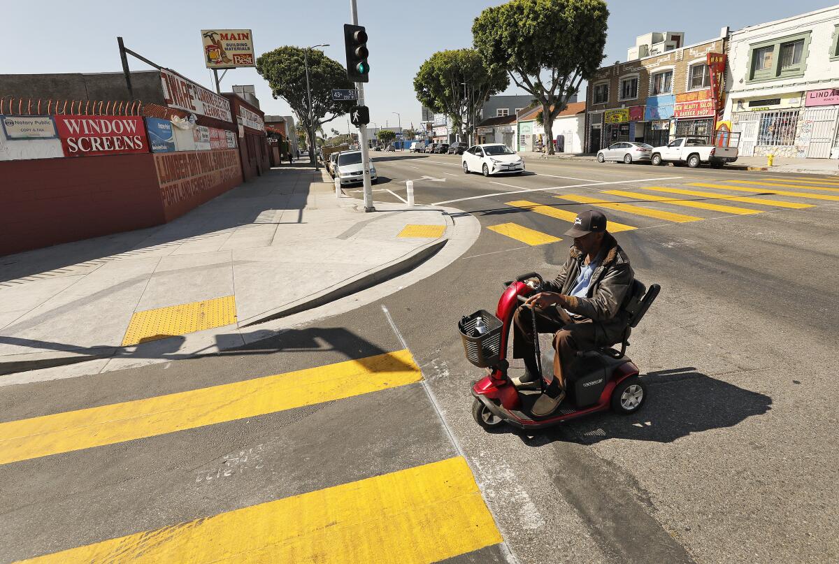 A person using a motorized wheelchair crosses a street with large crosswalks