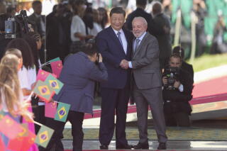 Two men in suits and ties smile while clasping hands as another man takes their photograph