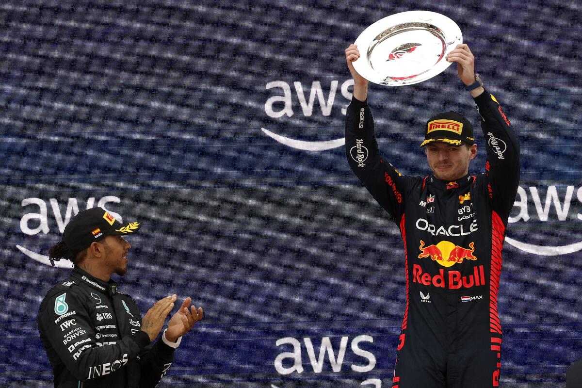 Lewis Hamilton applauds for winner Max Verstappen, who holds up a large silver plate.