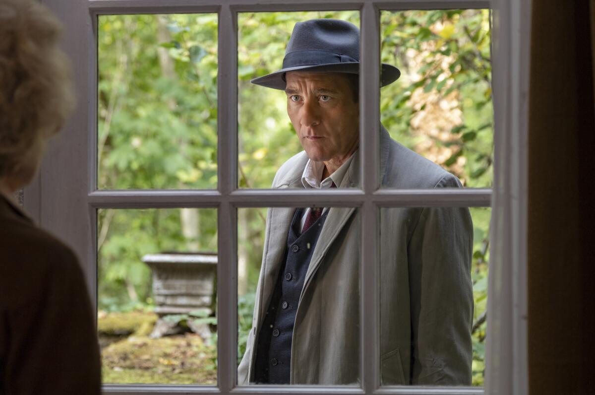 一个穿着大衣、戴着帽子的男人站在户外，透过窗户往外看。