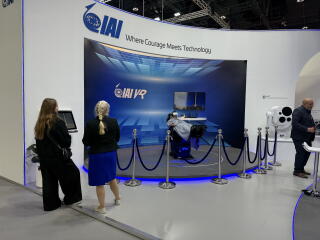 Two women stand looking at a display in a roped-off area with the letters IAI overhead