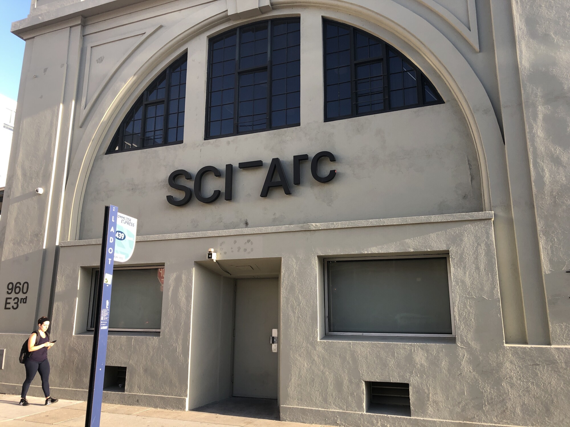 A woman walks in front of an old rail depot building bearing a sign for SCI-Arc.