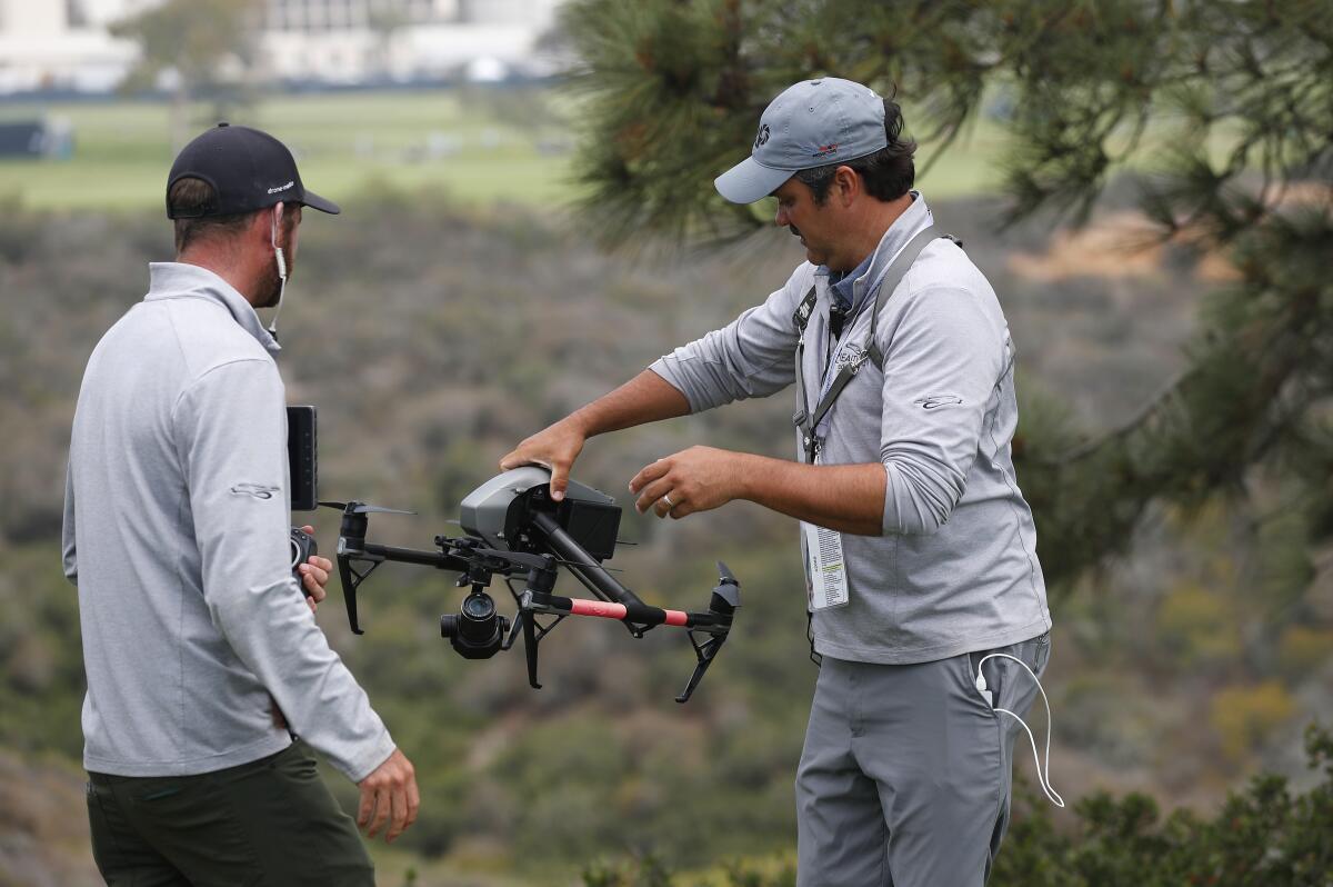 Drone operator Ben McClung picks up a drone used for coverage of the U.S. Open. Tanner Deprin, left, looks on.