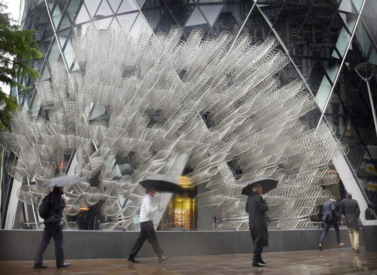 epa04933105 RECROP OF epa04933101 Pedestrians walk in the rain past the sculpture 'Forever' by Chinese artist Ai Weiwei outside the Gherkin building in London, Britain, 16 September 2015. The sculpture consists of 1.245 bicycle frames measuring 10 meters tall by 16 meters wide. EPA/FACUNDO ARRIZABALAGA ** Usable by LA, CT and MoD ONLY **