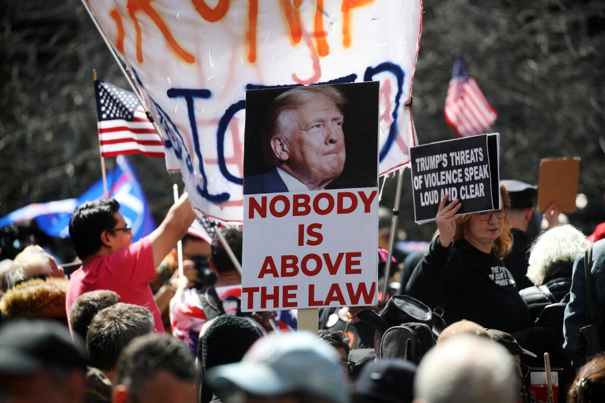 People gather outside Manhattan Criminal Court in New York with signs about Donald Trump