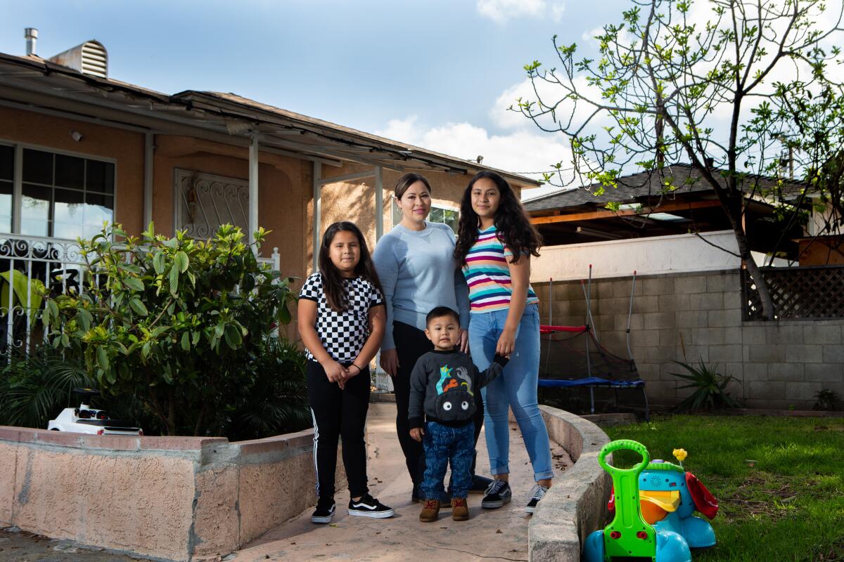 A mother and three children pose outside their home 