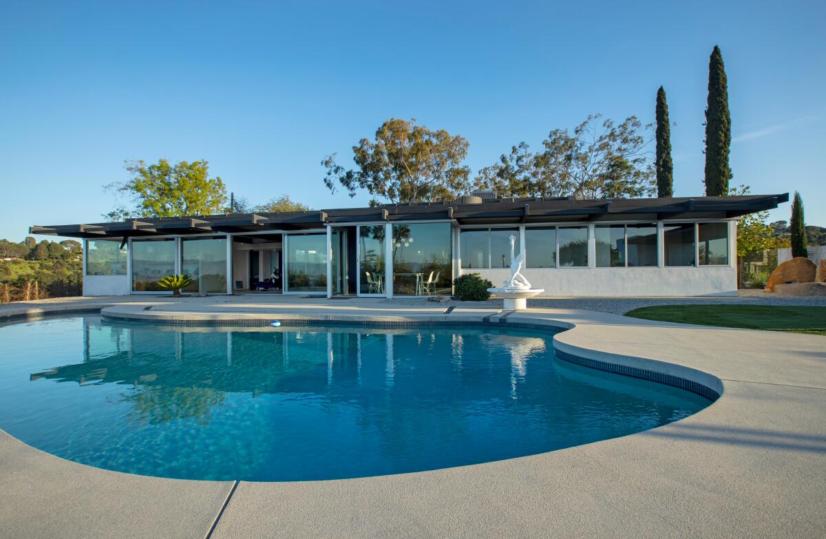 A Midcentury Modern home stands next to its swimming pool. 