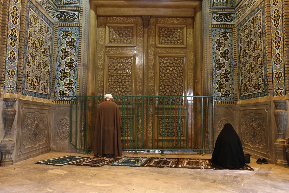 Two people pray March 16 behind a closed door at Masumeh shrine in Qom, 80 miles south of Tehran. Authorities closed the site, prompting angry demonstrations.