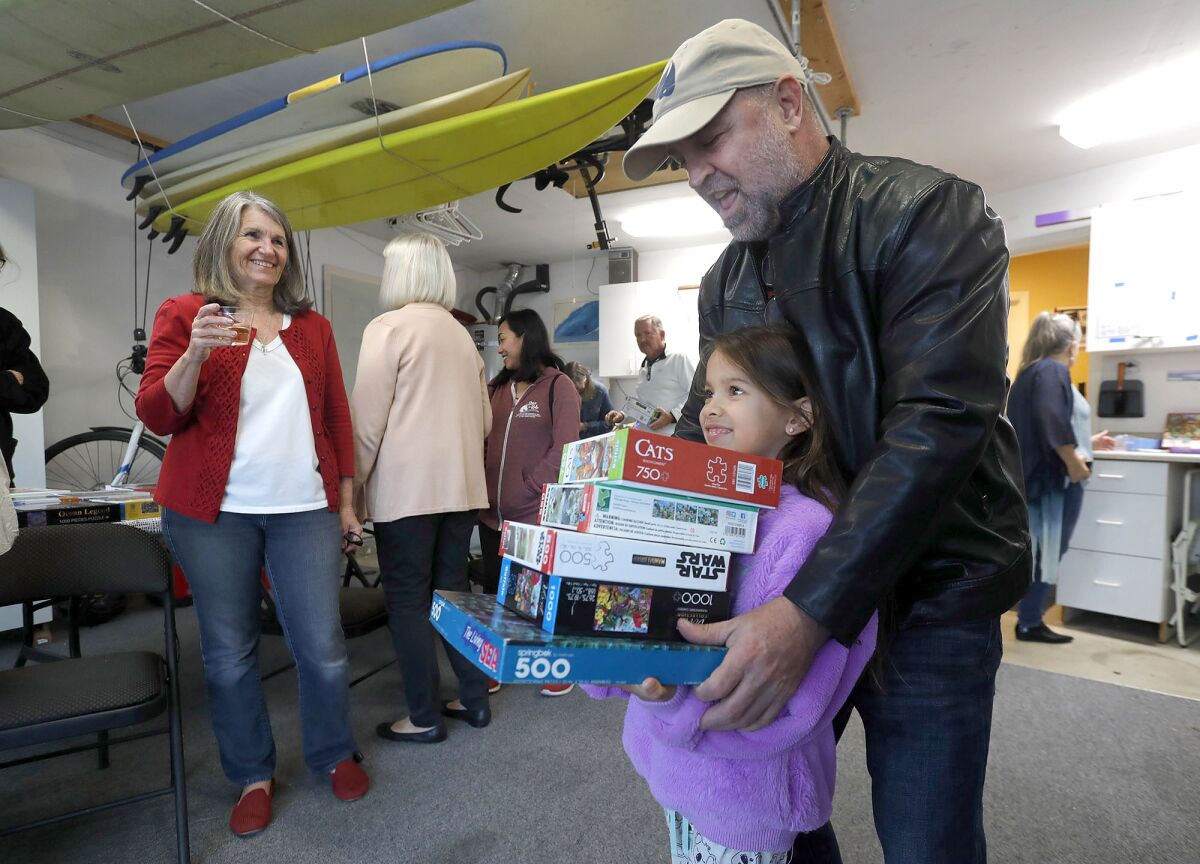 Puzzler Jazzlyn Lewis, with dad John, takes home a stack of puzzles Friday from the garage of Mary Fewel's Costa Mesa home.
