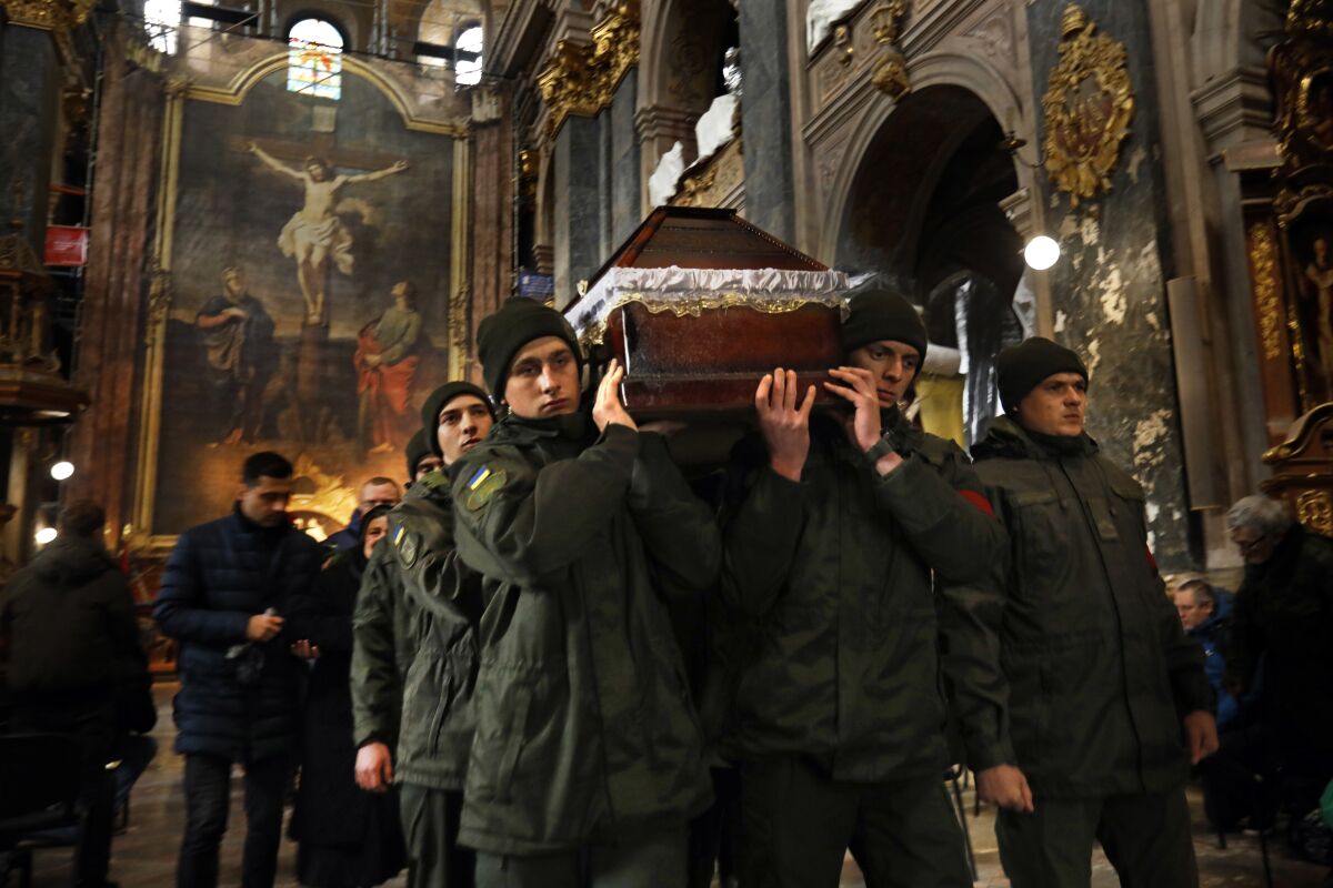 People in fatigues carry a coffin in a church with a painting of Christ on the cross in the background