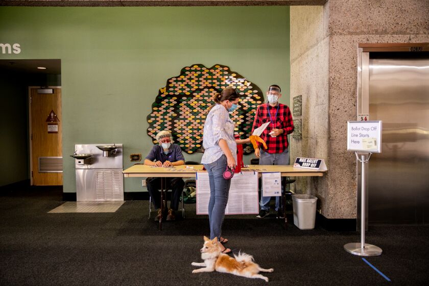 ESCONDIDO, CA - OCTOBER 20: Poll workers Carl Bennett and Evan Fallon help voter Tonja Phipps, alongside her dog Foxy, dropping off mail ballots for the 2020 Presidential General Election at the Escondido Public Library on Tuesday, Oct. 20, 2020 in Escondido, CA. (Sam Hodgson / The San Diego Union-Tribune)