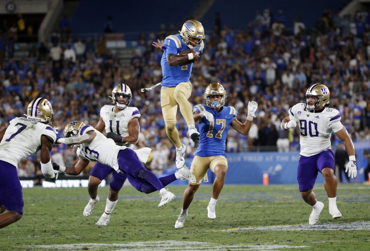 UCLA quarterback Dorian Thompson-Robinson leaps over Washington Huskies linebacker Kamren Fabiculanan for extra yardage.