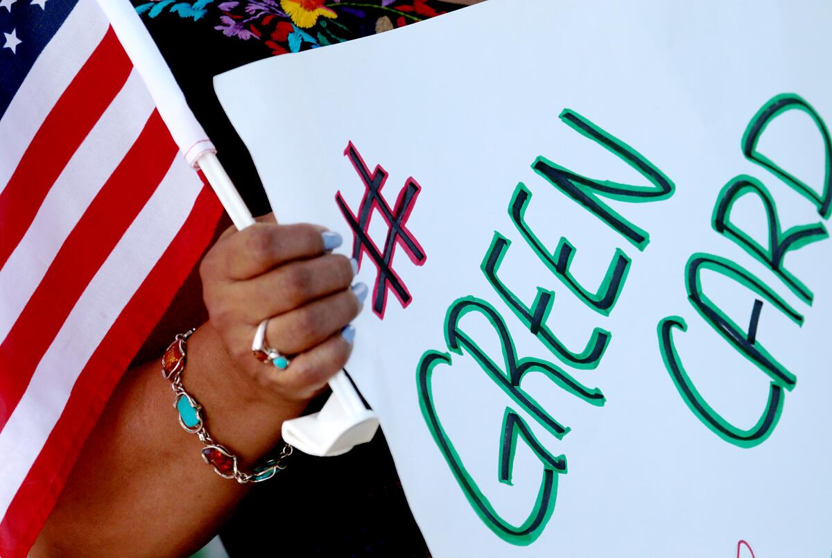 A demonstrator holds a sign that says # Green Card and a flag.