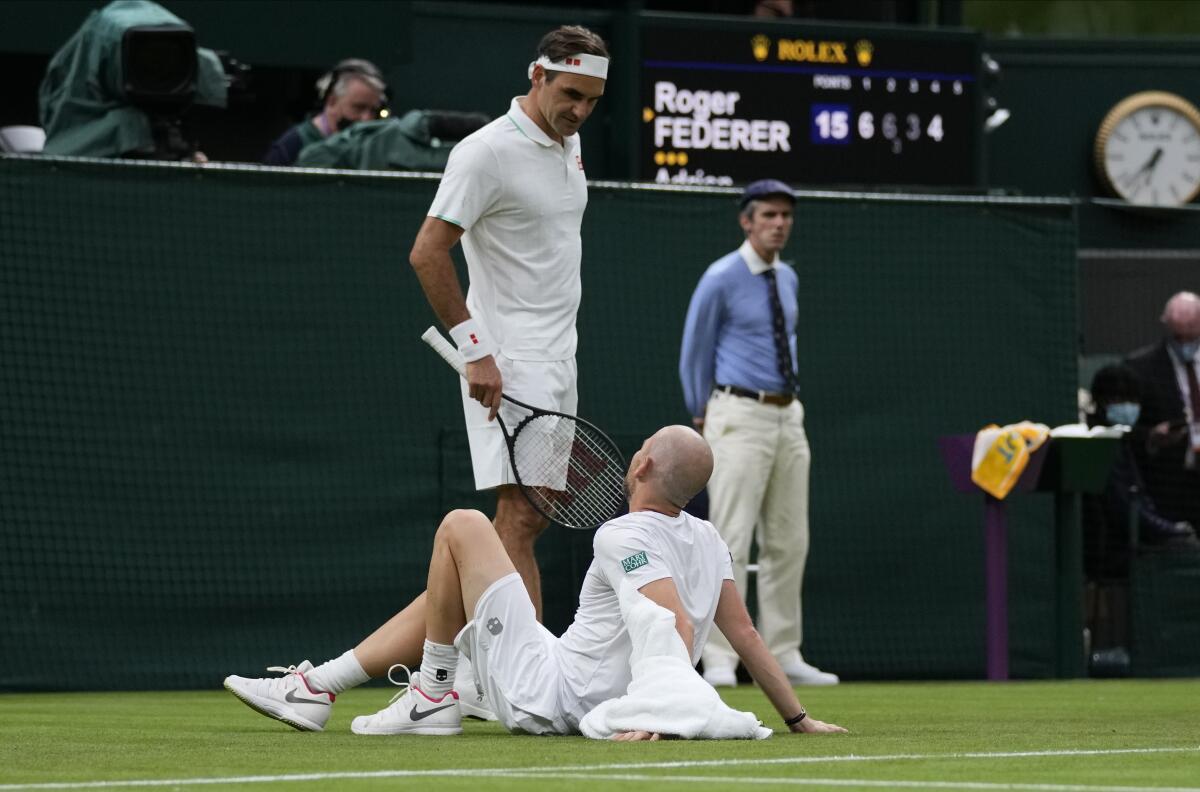 Roger Federer talks to Adrian Mannarino as he lies on the ground in pain during their first-round match.