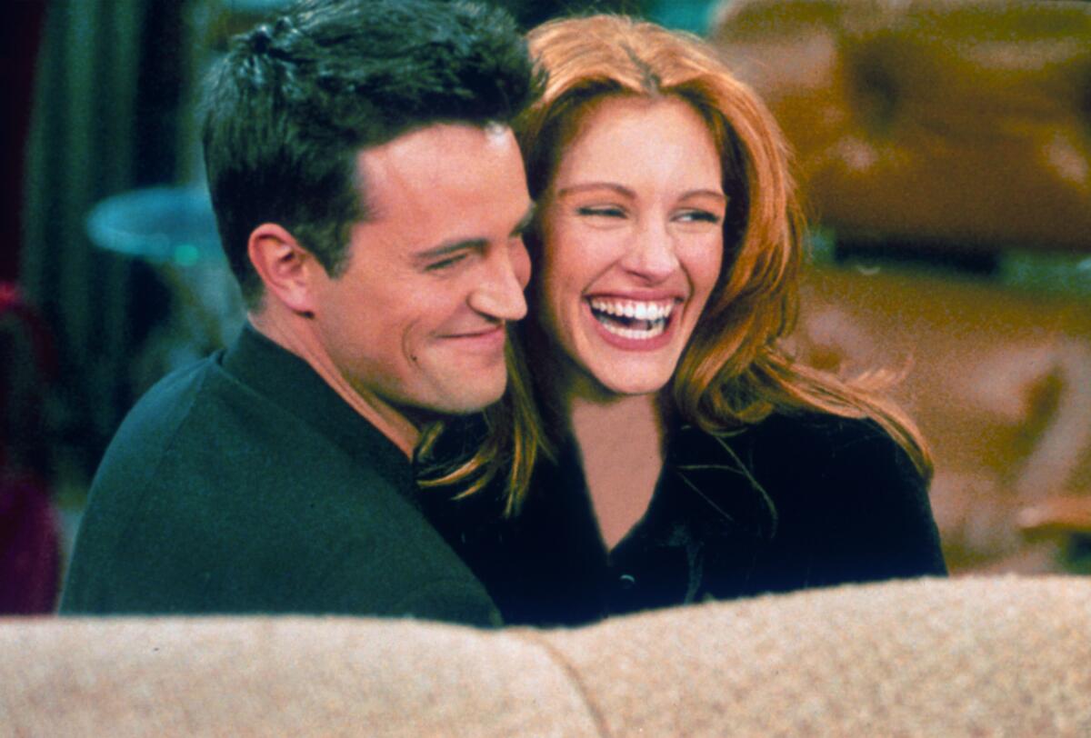 Matthew Perry and Julia Roberts, smiling wide, hug each other on the set of "Friends."