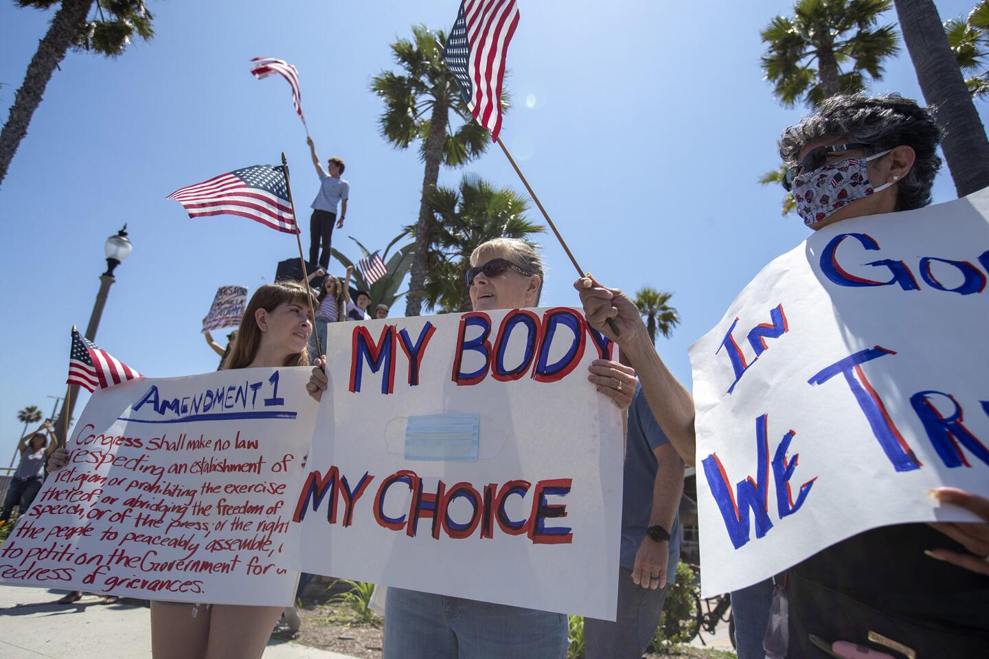 Madison Melendes, left, and Kelly Melendes, center and Priscilla Garcia, all from Costa Mesa, hold signs during a protest in Huntington Beach on Friday.