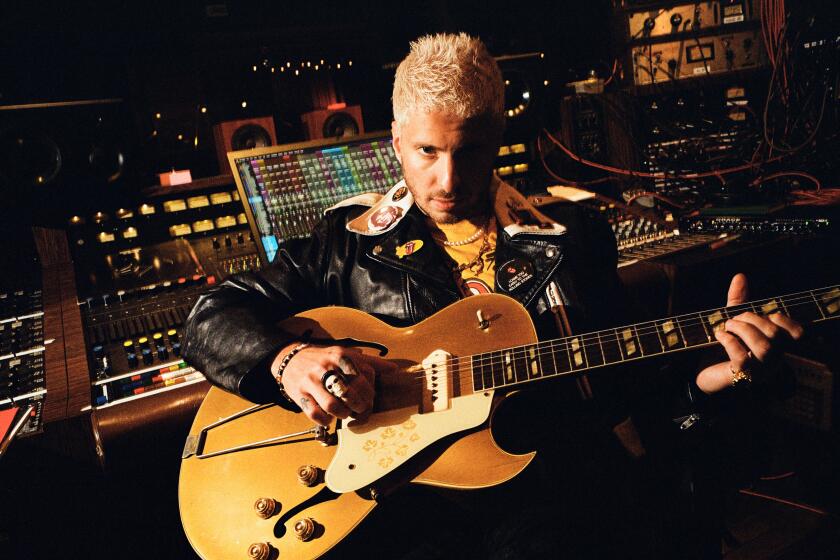 Man with bleached blond hair holding a guitar in a recording studio
