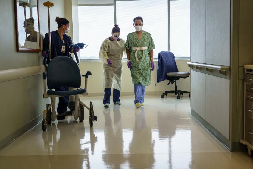 SAN DIEGO, CALIF. -- SATURDAY, APRIL 18, 2020: Don Udan, 32, with the assistance of his his physical therapist Justina Soultrain, center left, walks down the hallway at Sharp Memorial Hospital in San Diego, Calif., on April 18, 2020. (Marcus Yam / Los Angeles Times)