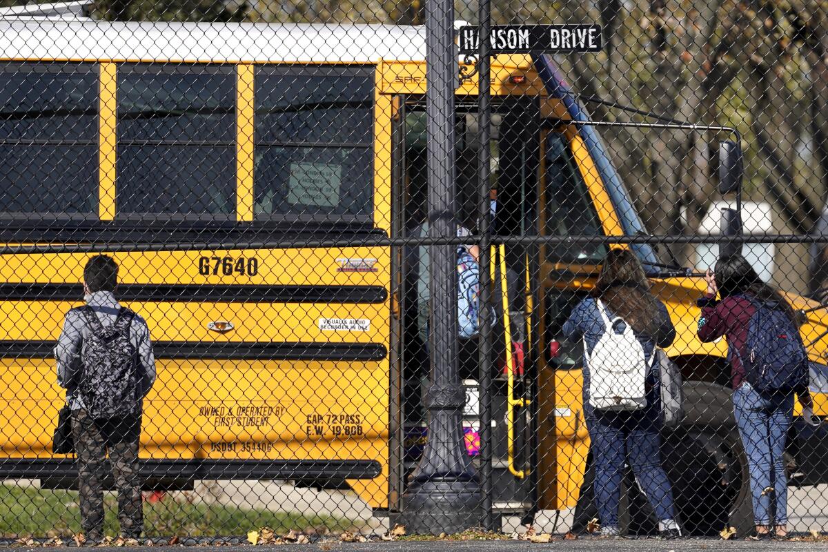 Kids wait to board a school bus behind fence