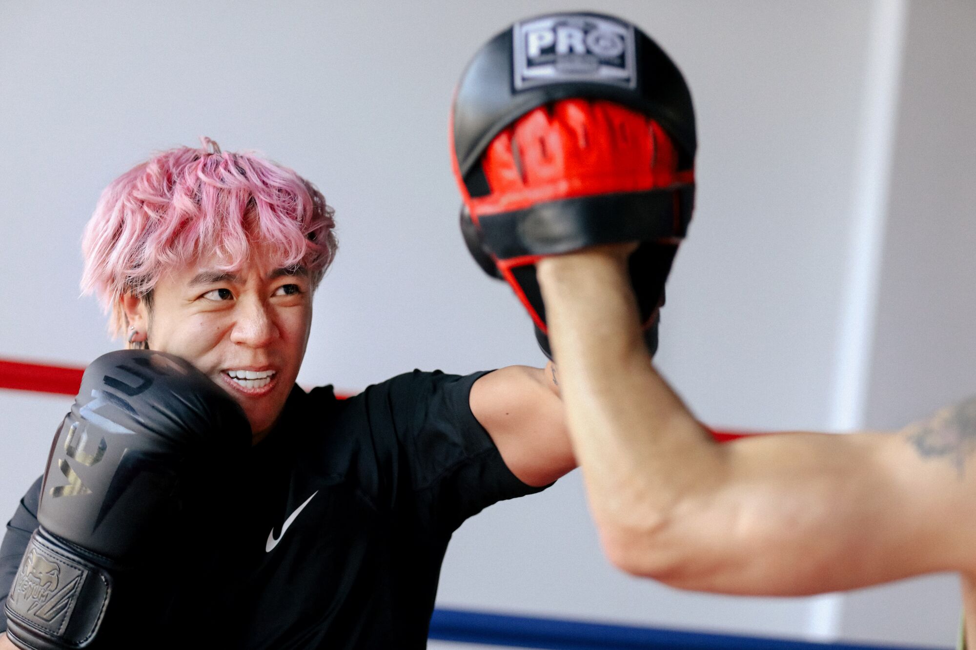 A boxer strikes his left glove against a trainer's mitt