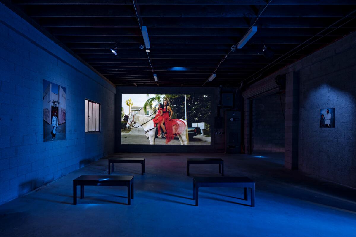 A screen in an empty room with chairs shows two women on a horse. 