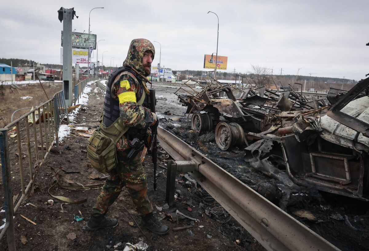 FILE - An armed man stands by the remains of a Russian military vehicle in Bucha, close to the capital Kyiv, Ukraine, March 1, 2022. (AP Photo/Serhii Nuzhnenko, File)