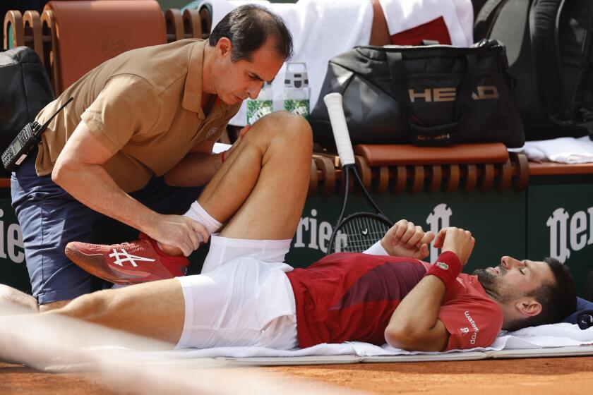 Serbia's Novak Djokovic lies on the ground with one knee up while receiving medical assistance on his knee.