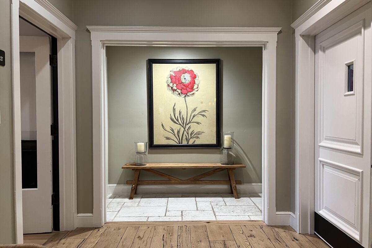 An interior hallway in a hote, with white doors and frames and a floral painting on the muted green wall