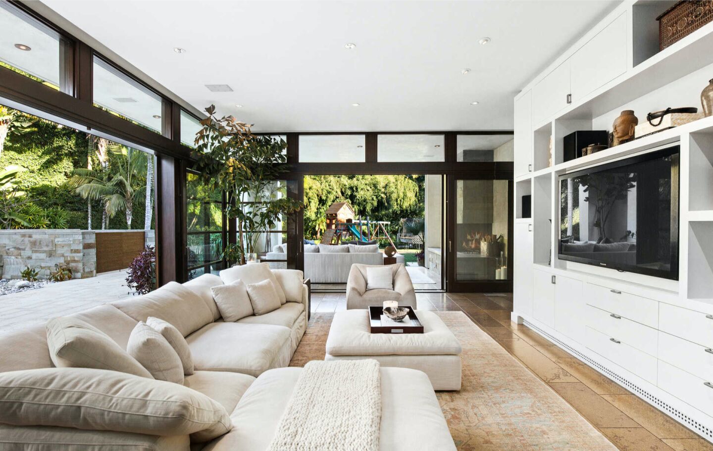 The furnished family room with a built-in TV and big windows looking out on trees.