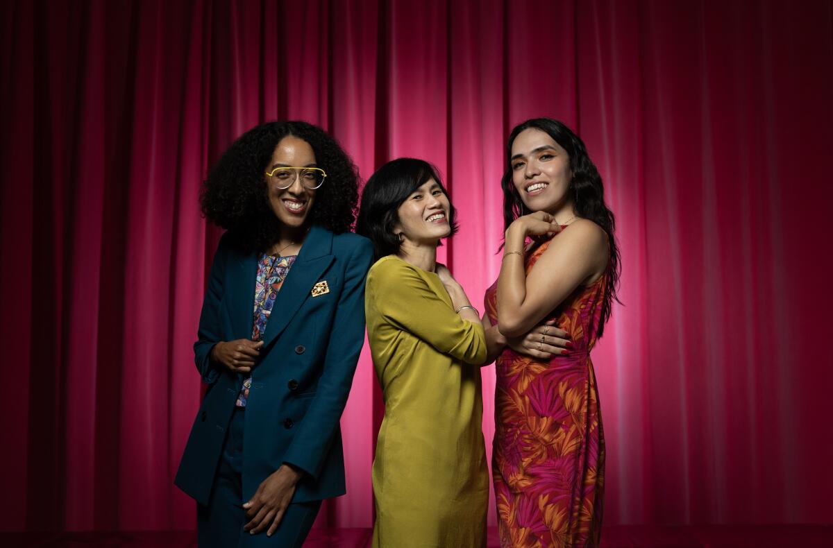 Three people smile for the camera in front of a curtain.