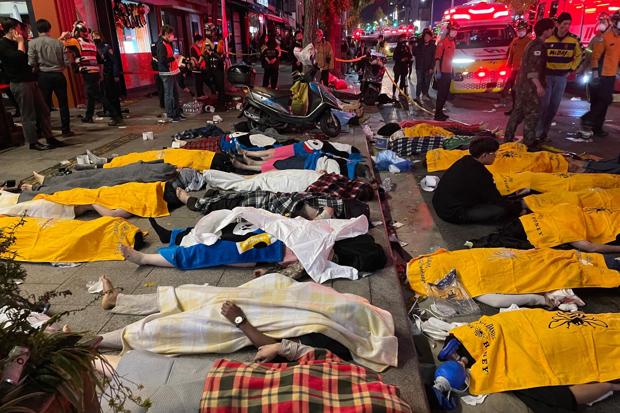  About 20 bodies lie covered on a street 