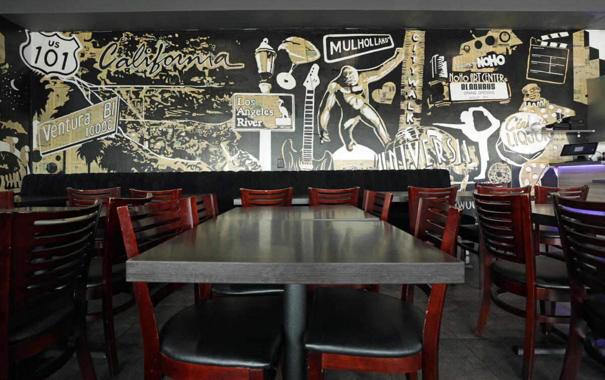The interior of a restaurant with family-style tables and a mural on the wall of California landmarks.