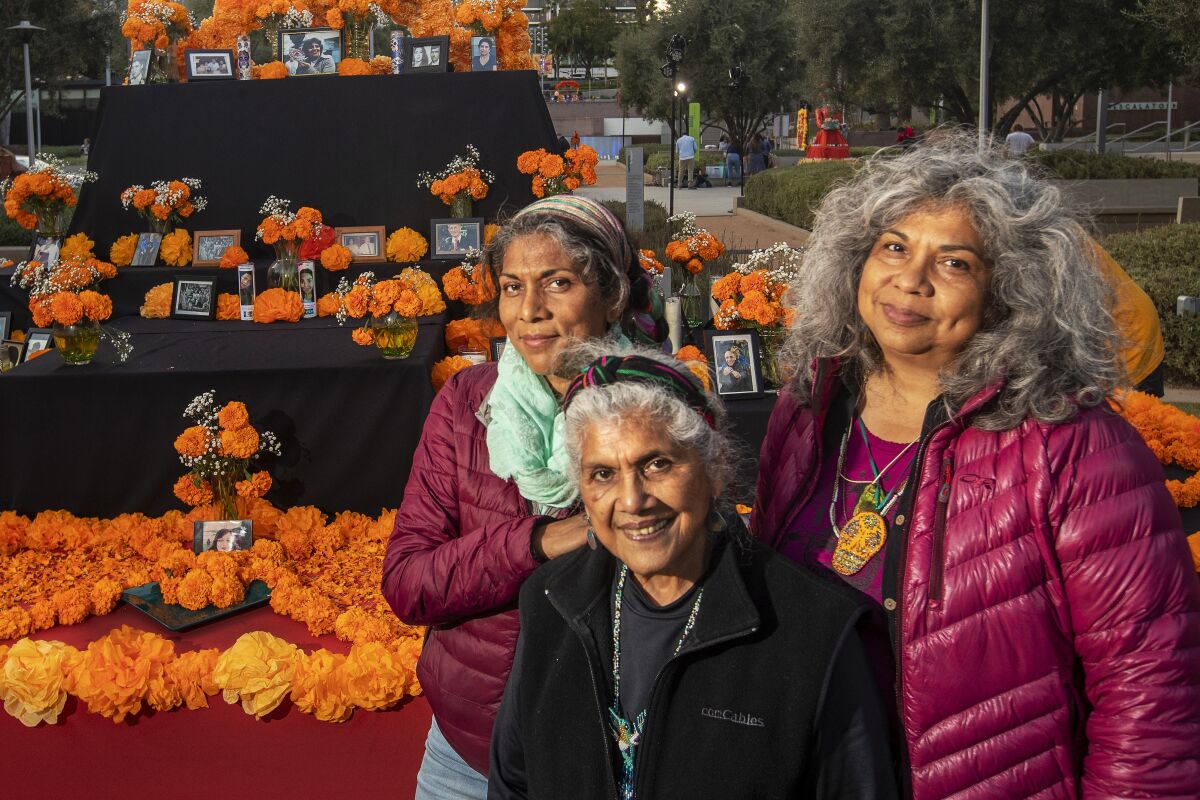 Three women before a colorful altar covered in marigolds