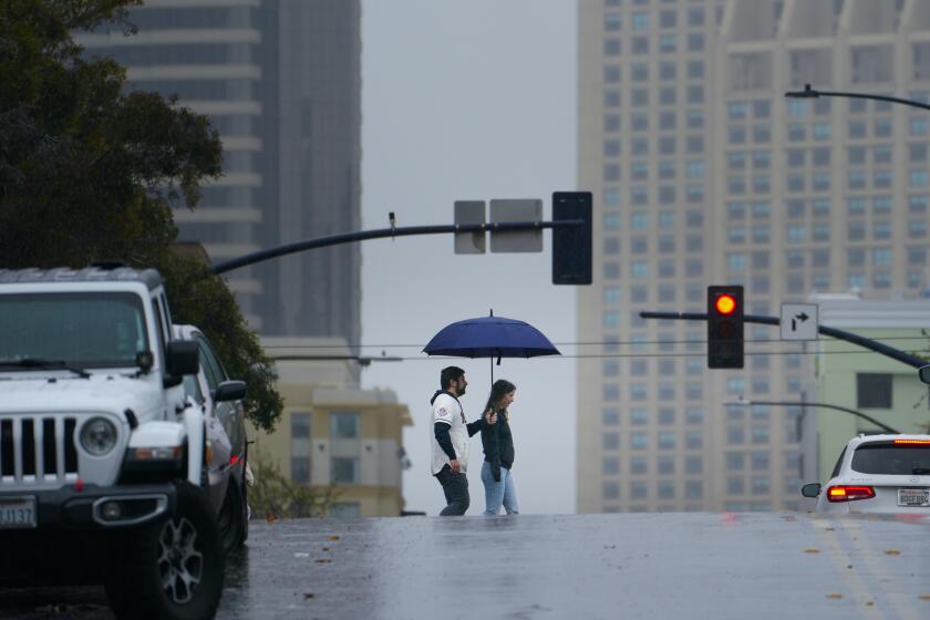 San Diego, CA - March 30: On a rainy afternoon, two people share an umbrella as they cross J Street in downtown’s East Village on Saturday, March 30, 2024, in San Diego, CA. (Nelvin C. Cepeda / The San Diego Union-Tribune)