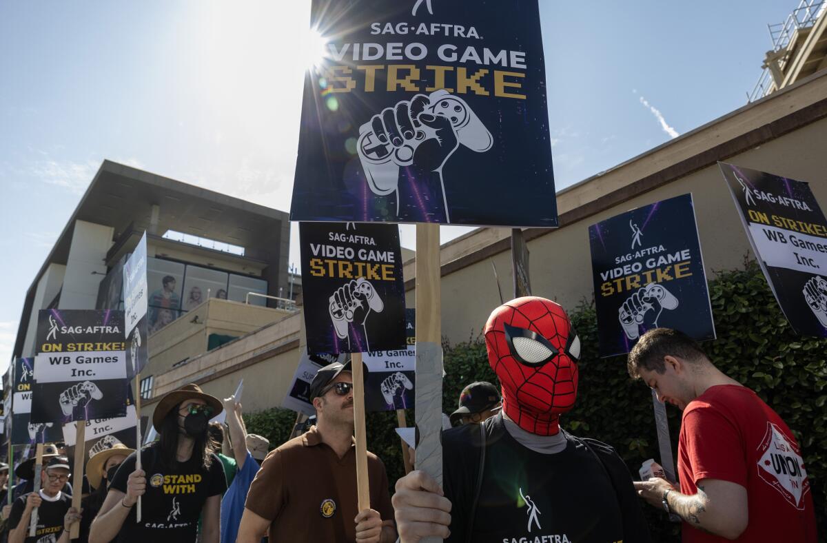 A person in a Spider-Man mask marching in a group and carrying a picket sign that reads "SAG-AFTRA video game strike"