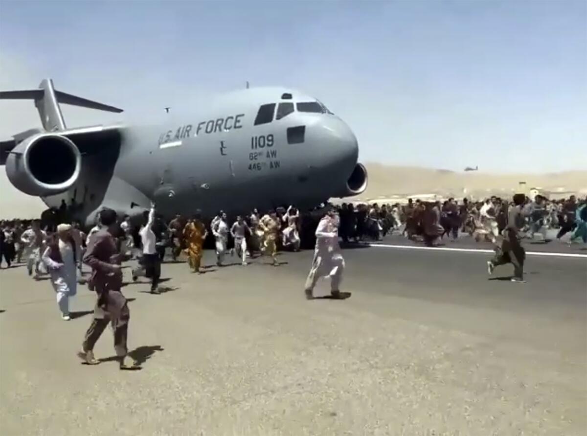 Hundreds of people run alongside a U.S. Air Force transport plane as it moves down a runway.