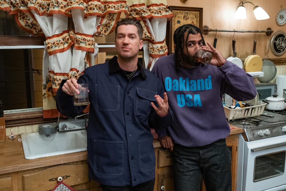 Two men in a kitchen drinking and looking at the camera