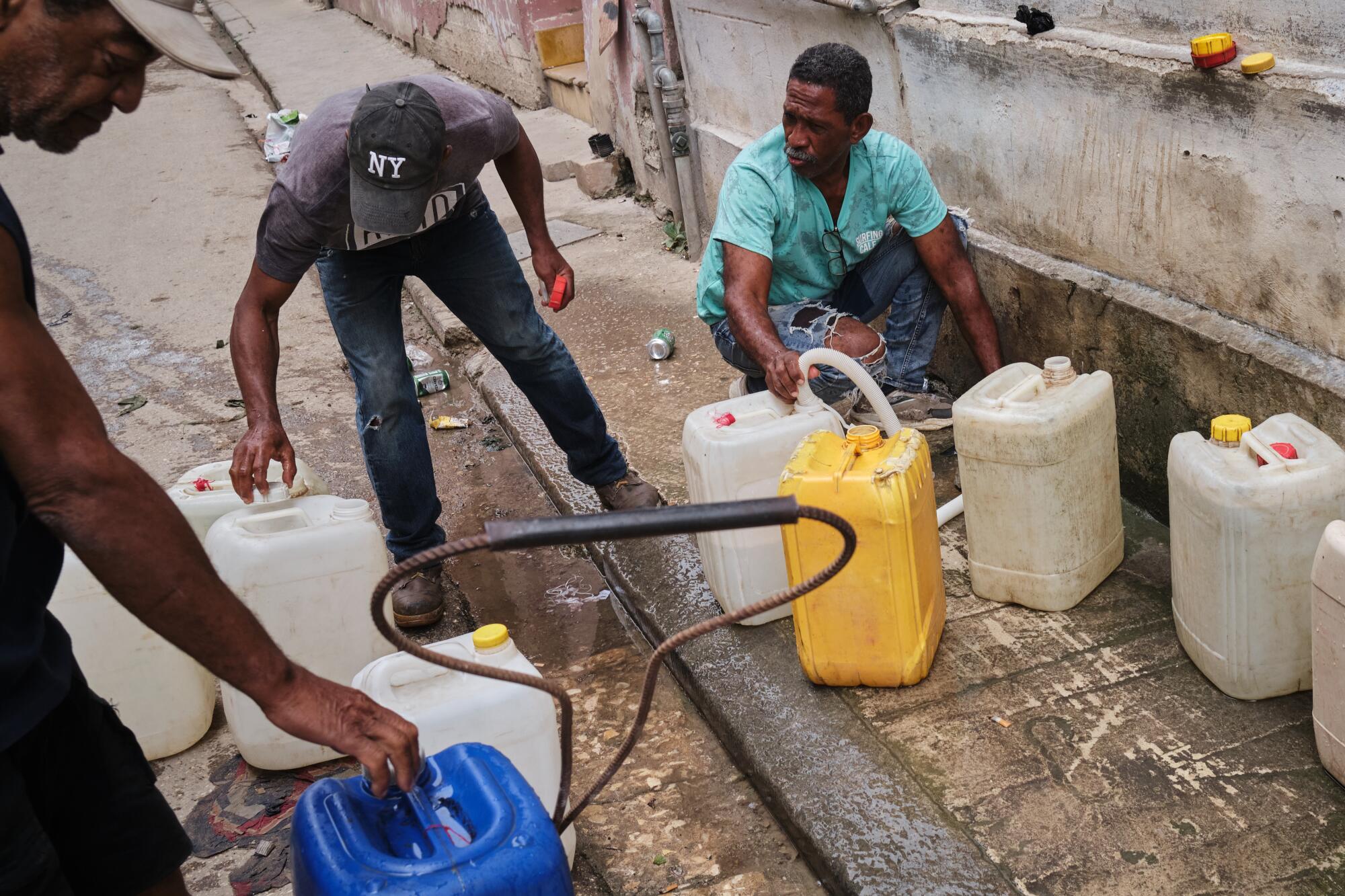 Men fill plastic containers with water on a sidewalk.