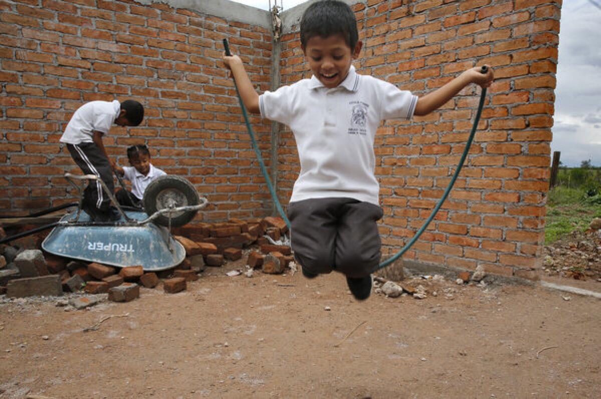 Carlos Ireta uses a garden hose as a jump rope as Noe and Teresa play in the unfinished living room of their future house near Irapuato, Mexico.