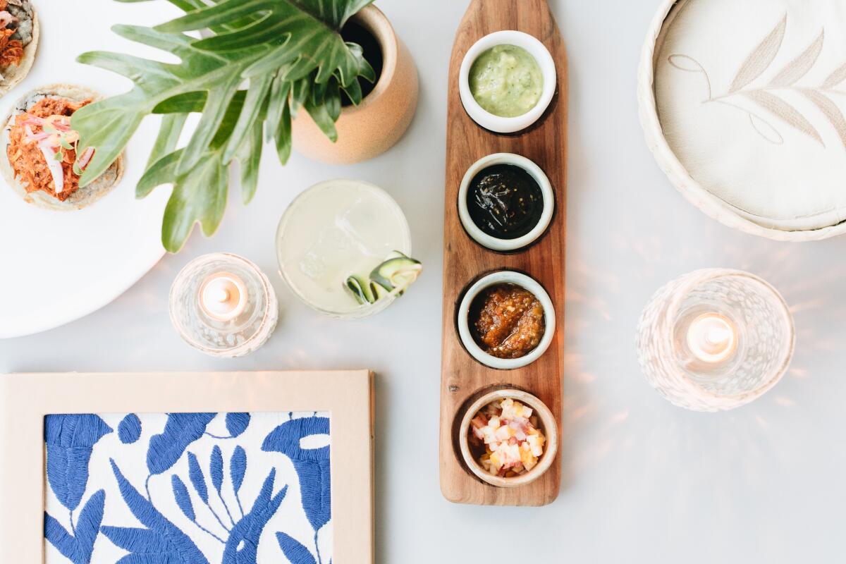 An overhead photo of tacos, a sampler of salsas, and a cocktail.