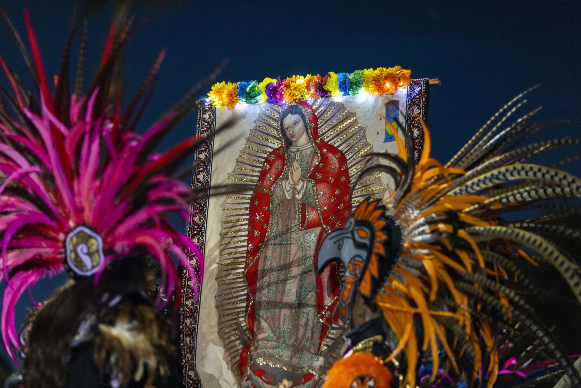 Images of La Virgen de Guadalupe are displayed during an Aztec dance.