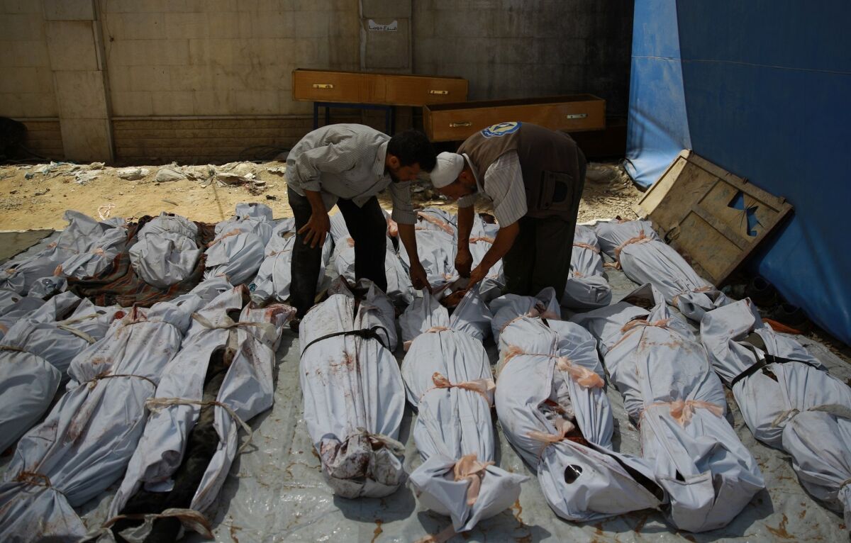 A Syrian emergency worker and a civilian inspect the bodies wrapped in plastic bags outside a makeshift hospital in the rebel-held area east of the capital Damascus, following reported airstrikes by regime forces on Aug. 12, 2015, that reportedly killed at least 27 people. The attack came after rebel rocket and mortar fire hit Damascus.