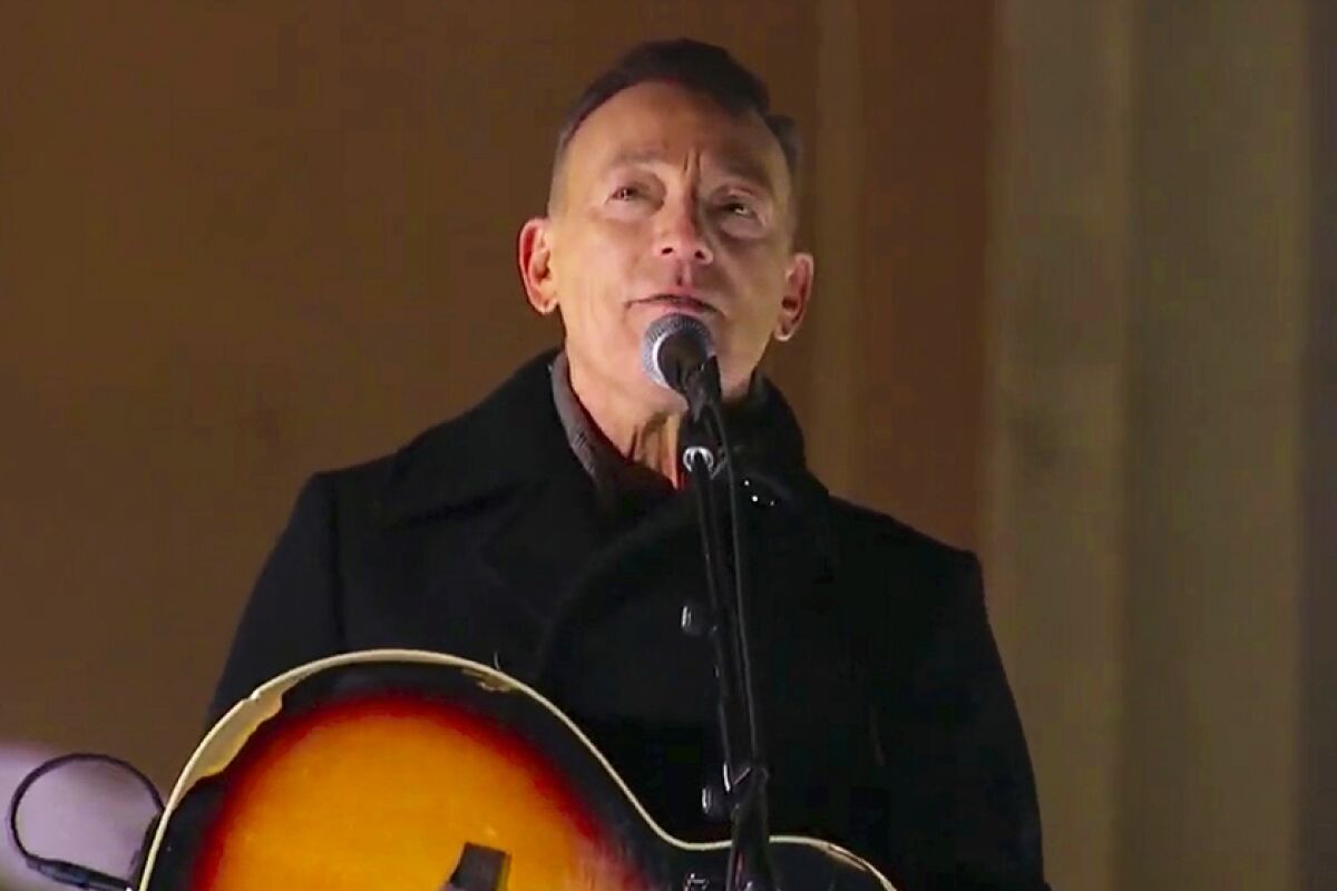 A man in a black coat holding an acoustic guitar.