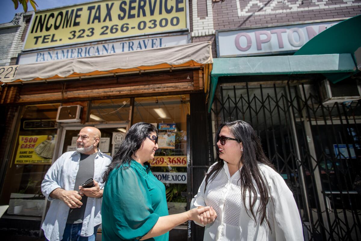 Wendy Carrillo, right, talks with Brenda Martinez, while Jorge Martinez stands, left, in front of shops.