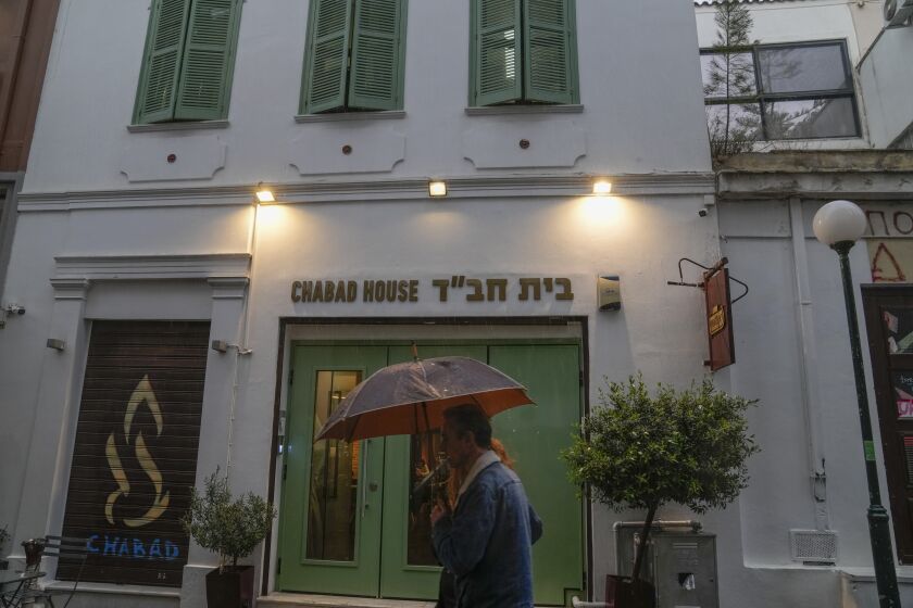 A man holding an umbrella walks past a Jewish restaurant that Greek officials believe was one of the targets of a planned terrorist attack, in central Athens, Tuesday, March 28, 2023. Greek police said Tuesday they have arrested two terrorism suspects with Pakistani origin, who had been planning attacks in the country aimed at causing mass casualties. (AP Photo/Thanassis Stavrakis)