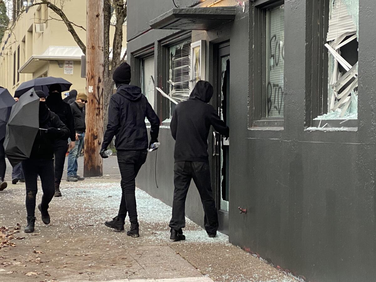 A person dressed in black stands next to a building amid broken glass