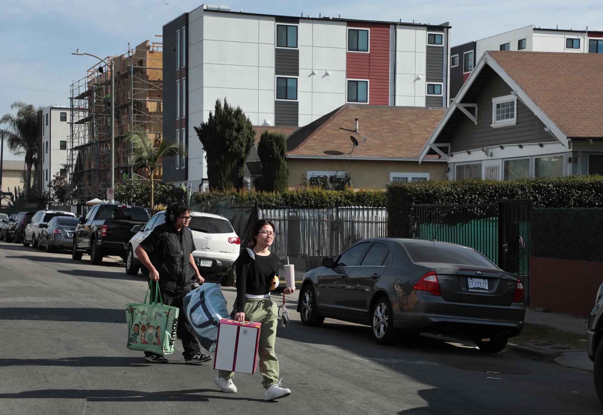 Two people carrying bags cross a residential street.