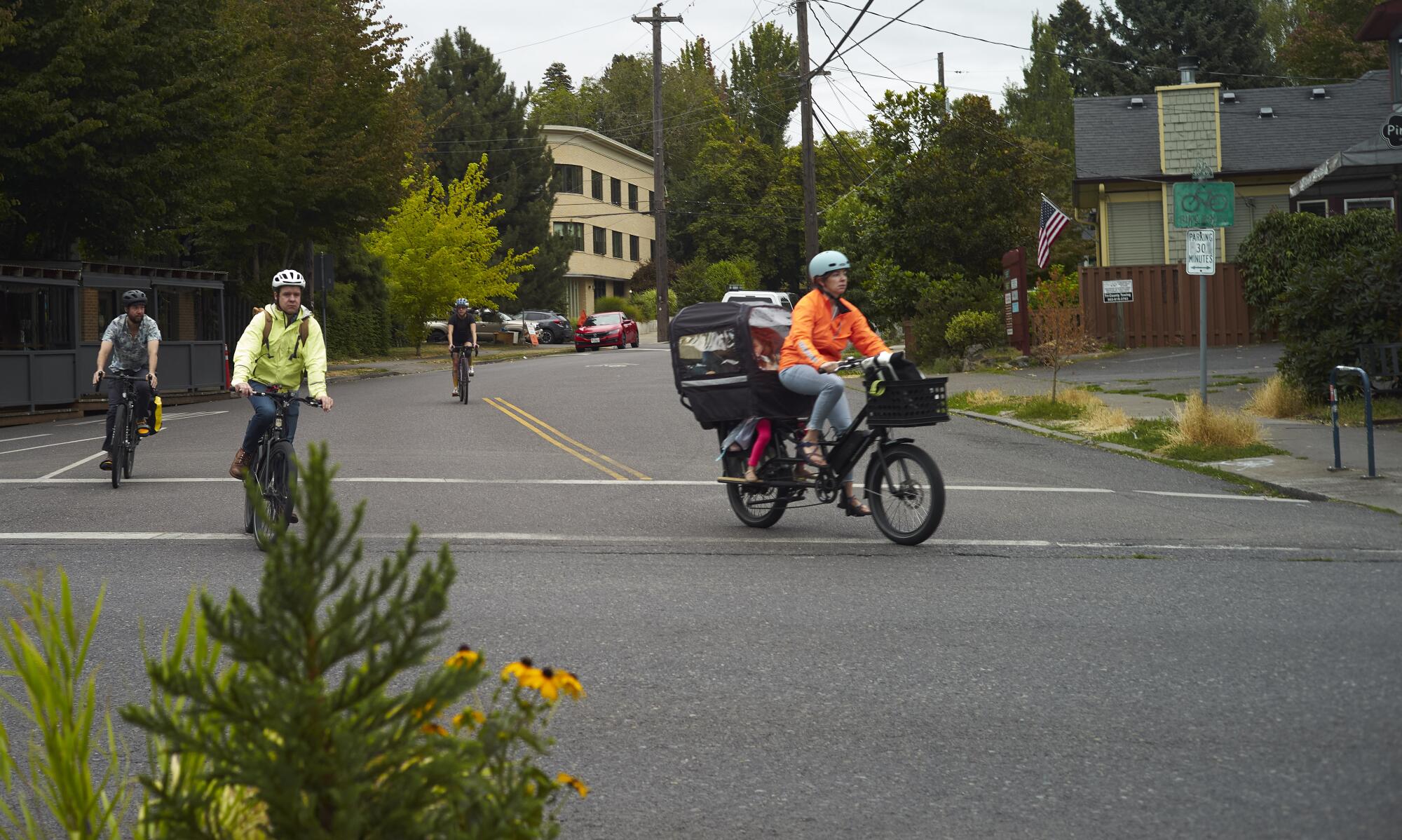 Four cyclists, riding different types of bikes, peddle down a tree-lined city street. 