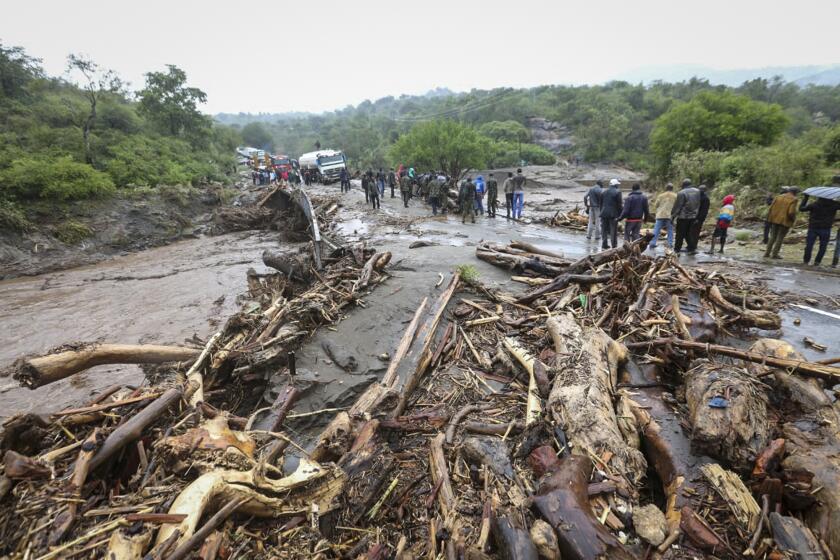 Passengers from stranded vehicles stand next to the debris from floodwaters, on the road from Kapenguria, in West Pokot county, in western Kenya Saturday, Nov. 23, 2019. Kenya's interior minister says dozens of people have been killed in mudslides, after heavy rains unleashed overnight floods in western Kenya. (AP Photo)