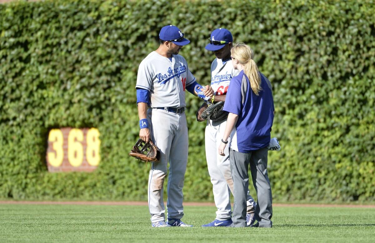 Dodgers center fielder Andre Ethier, left, and team trainer Sue Falsone look at right fielder Yasiel Puig's left hand after he made a diving catch in the seventh inning of Saturday's win over the Chicago Cubs.